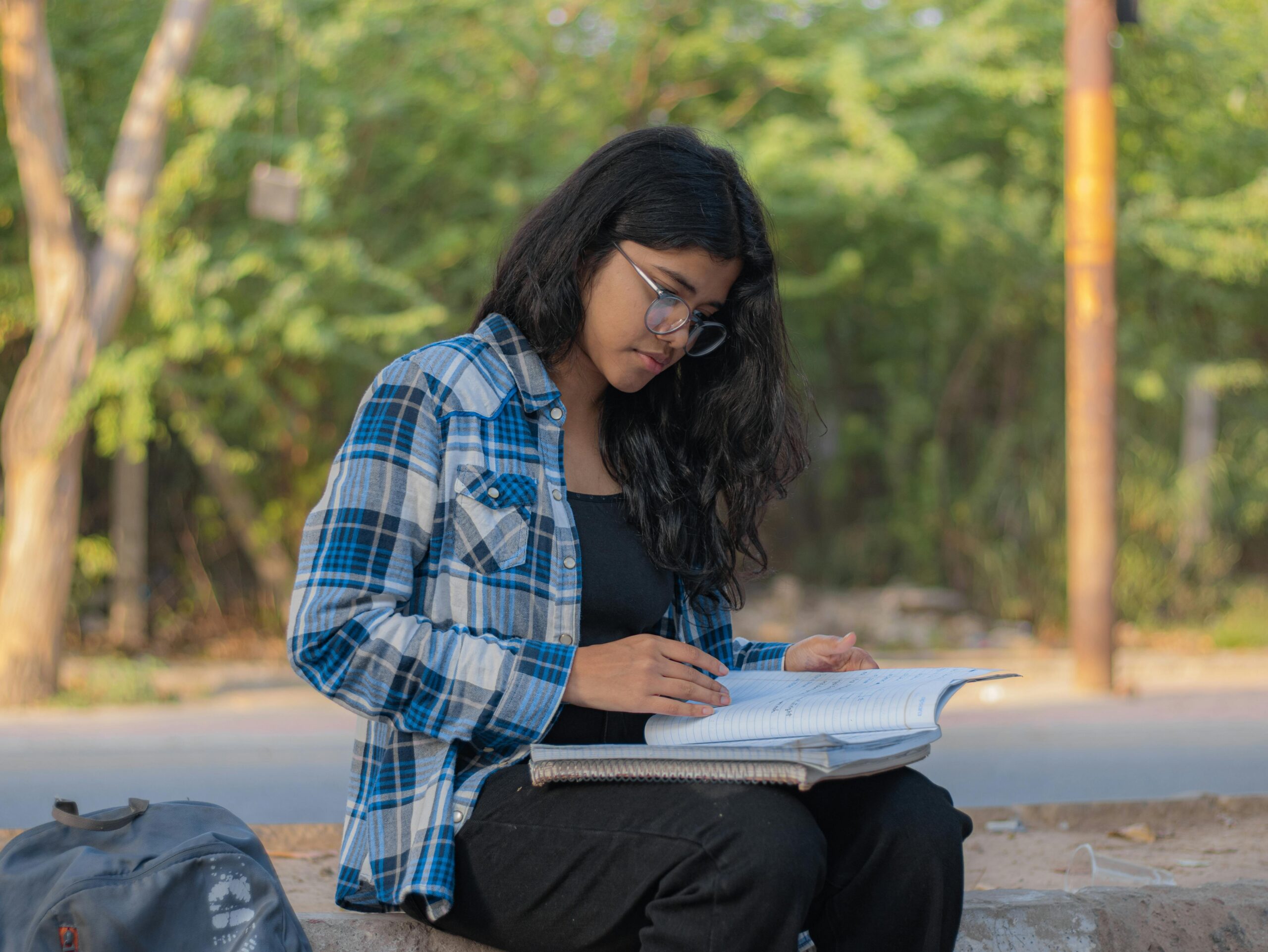 Young woman reading and studying with notebook outdoors on a sunny day.